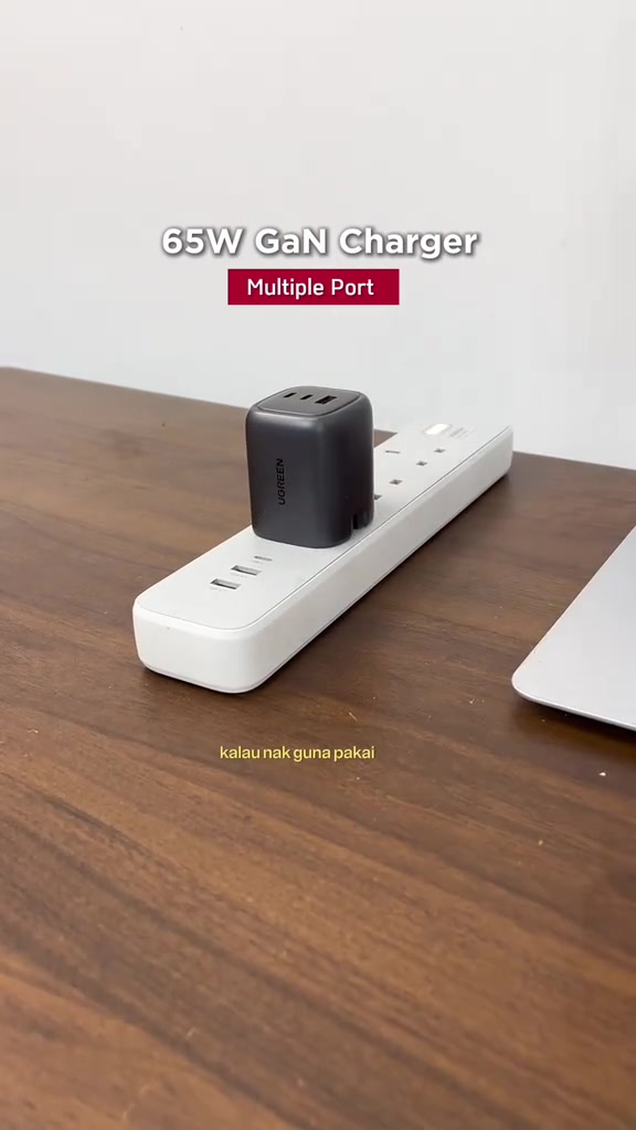 Pengecas UGREEN 65W warna hitam dipasang pada strip soket putih di atas meja kayu
