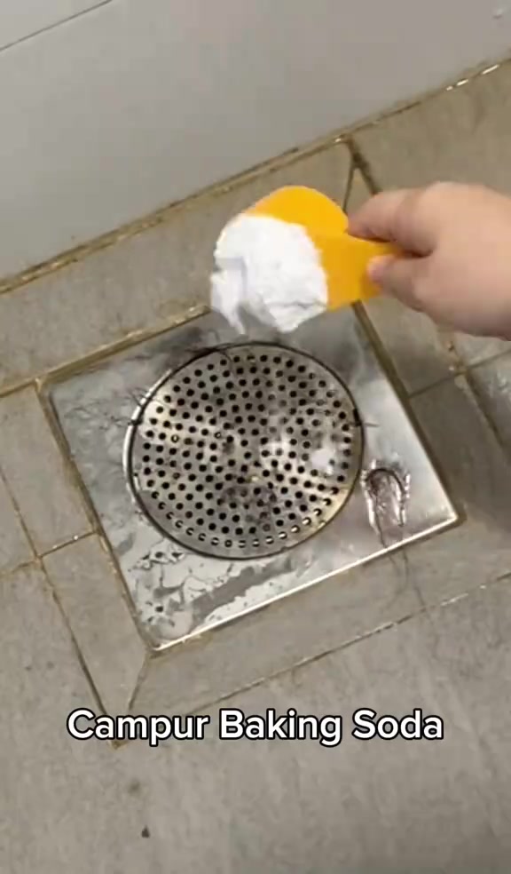 Tangan menabur baking soda guna penyodok kuning ke atas floor trap berlubang di lantai bilik air