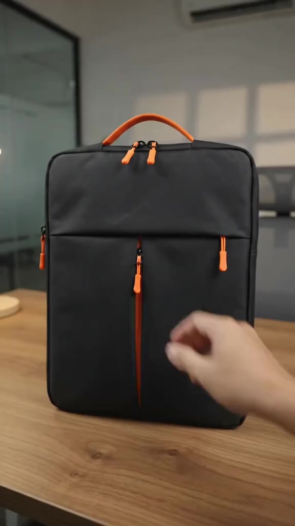 Beg laptop jenis berpemegang warna hitam dengan zip dan handle jingga berdiri tegak di atas meja kayu