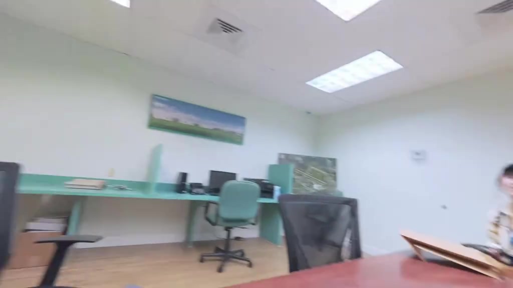 Văn phòng trường bay với bàn ghế và kệ hồ sơ màu xanh xuất hiện trong vlog, nơi cặp đôi ghé lại cảm ơn ê-kíp cũ