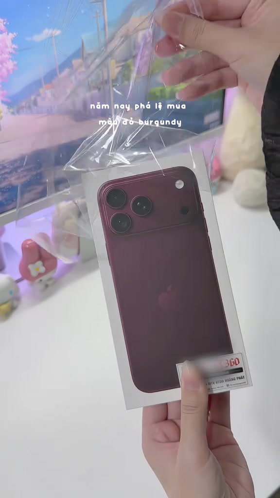 Mặt lưng iPhone 18 Pro Max màu đỏ burgundy với dải kính ngang ba ống kính, còn nằm trong túi nilon của hộp
