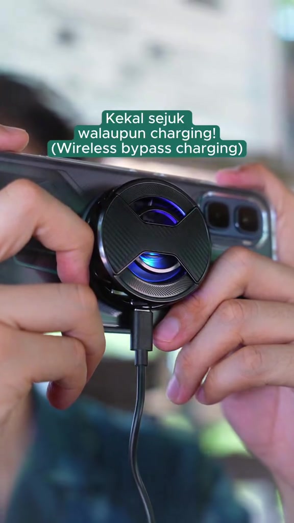 Cooler magnet bulat dengan lampu biru dipasang pada belakang phone gaming sambil dicas melalui wayar