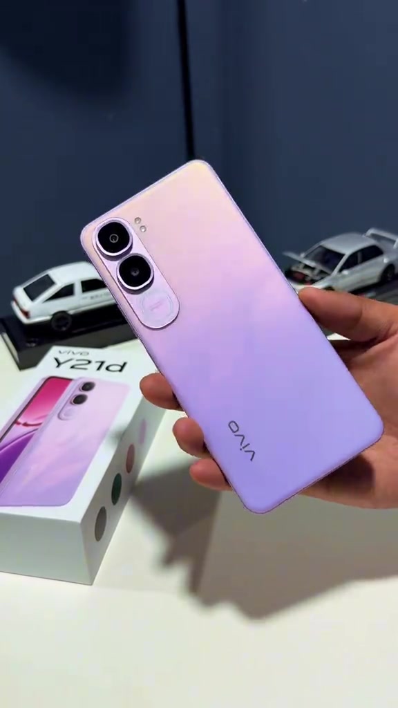 Belakang vivo Y21d warna ungu pudar dipegang sebelah tangan, kotak putih bertulis vivo Y21d kelihatan di latar