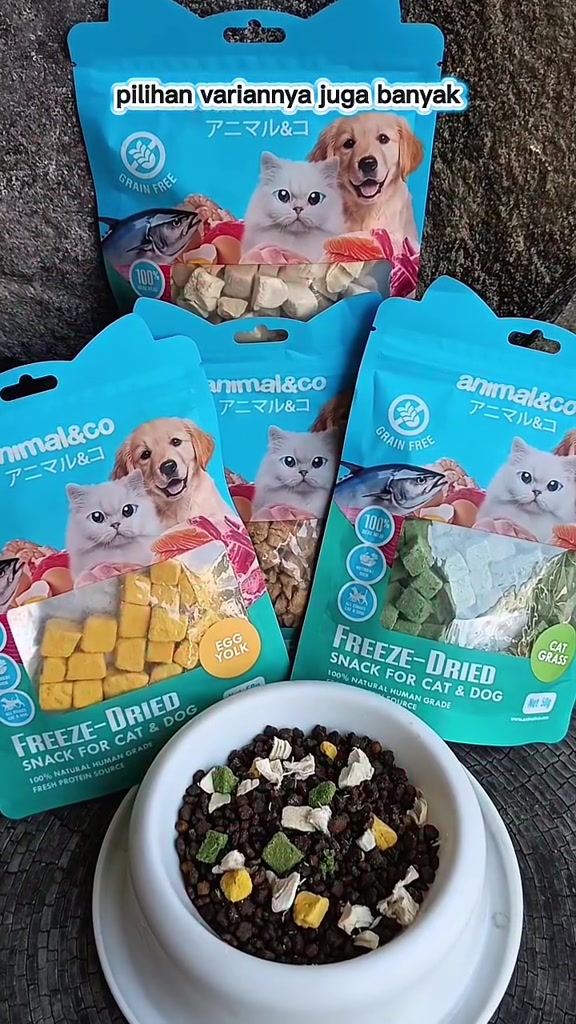 Mangkuk putih berisi kibble ditabur kiub freeze-dried hijau, kuning dan putih dengan pek Animal&Co di belakang