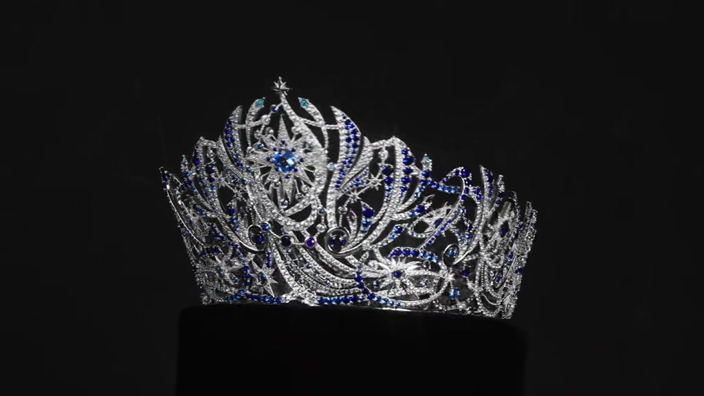 Vương miện Miss Universe Vietnam 2026 với đá trắng và xanh lam đặt trên bục đen, nền tối