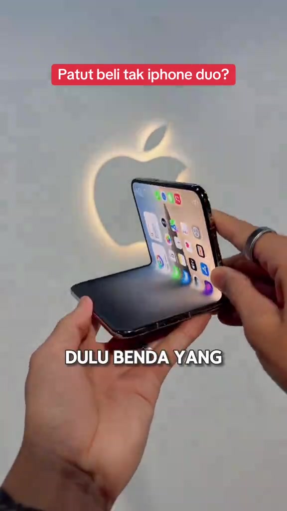 iPhone Duo dibuka separuh dipegang dua tangan di hadapan logo Apple bercahaya