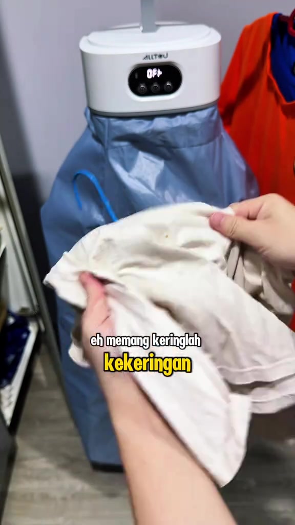Tangan memegang baju putih yang baru kering dikeluarkan dari mesin pengering portable