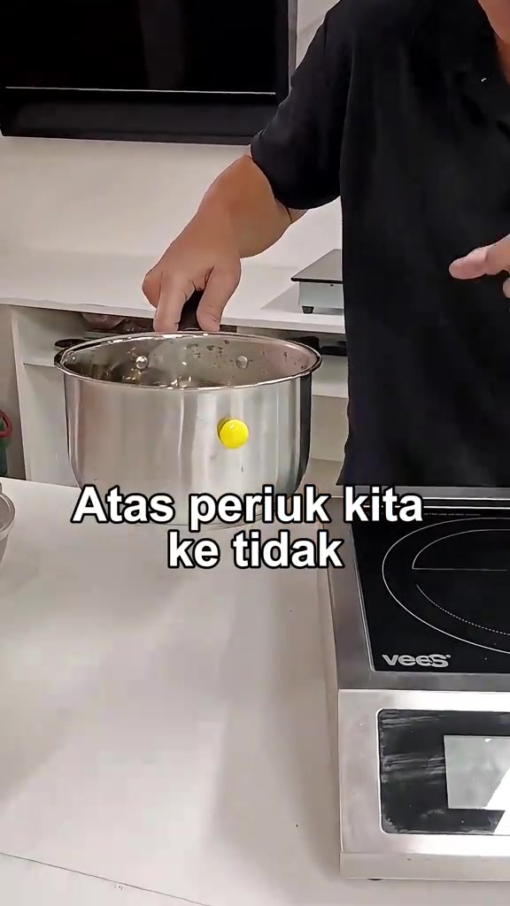 Tangan melekatkan magnet kuning pada sisi periuk stainless steel di sebelah dapur induction untuk uji kesesuaian