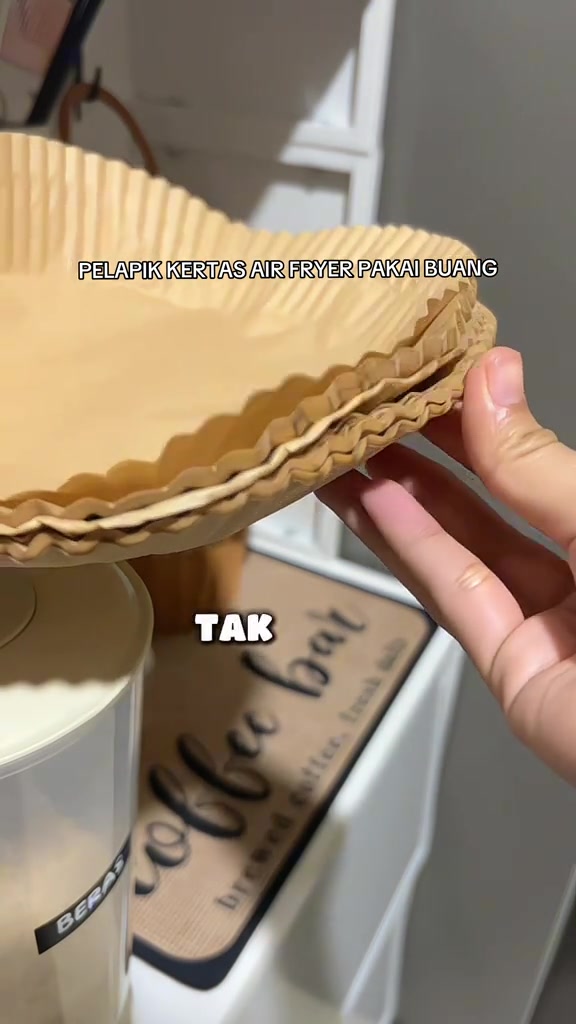 Tangan memegang timbunan pelapik kertas air fryer bulat warna kraft menunjukkan beberapa keping bertindih