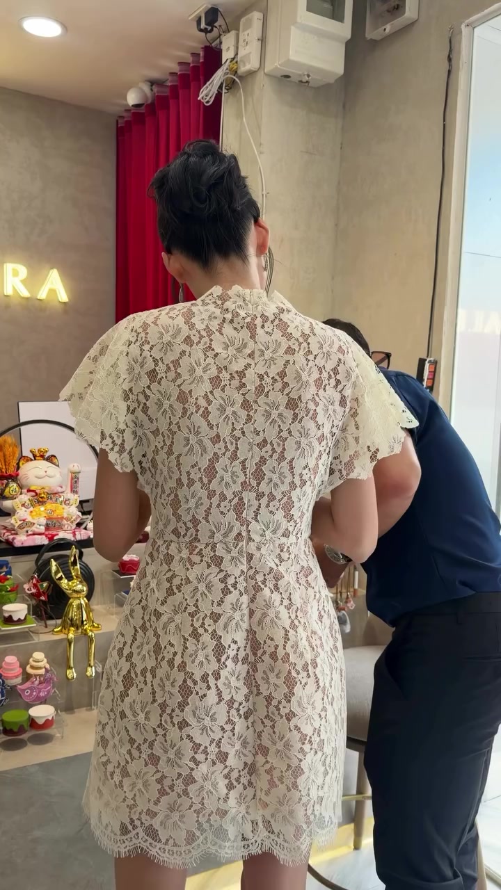 Quầy trưng bày charm và phụ kiện bên trong cửa hàng Alex & Sara, chụp từ phía sau hai người đang đứng nên không thấy khuôn mặt, phía xa là rèm đỏ và biển tên cửa hàng