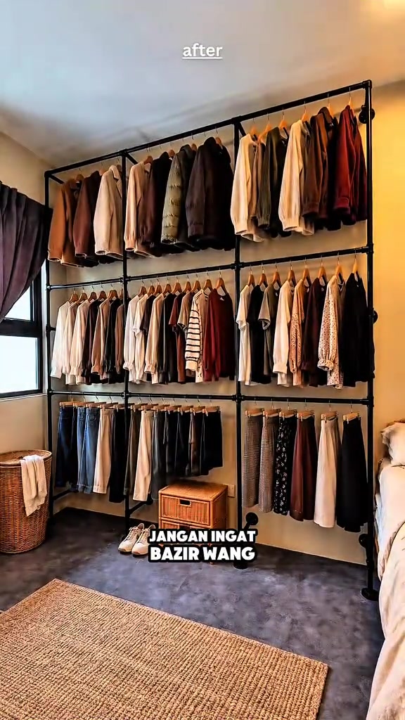 Open wardrobe besi hitam tiga tingkat penuh dengan baju bergantung pada penyangkut kayu di dinding bilik tidur
