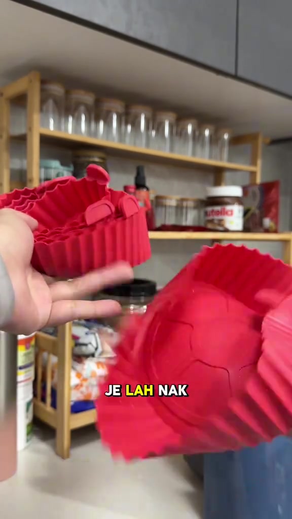 Tangan memegang pelapik silikon air fryer merah yang dilipat menunjukkan ia boleh disimpan nipis di dapur
