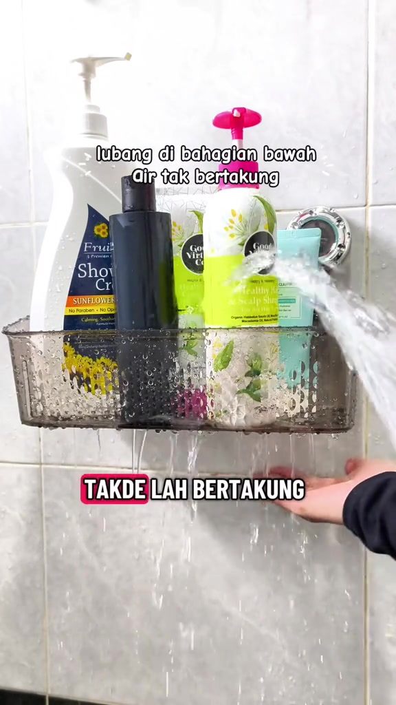 Rak cawan sedut berwarna kelabu di dinding jubin bilik air berisi botol syampu dan pencuci, air mengalir keluar melalui lubang tapisan di dasarnya