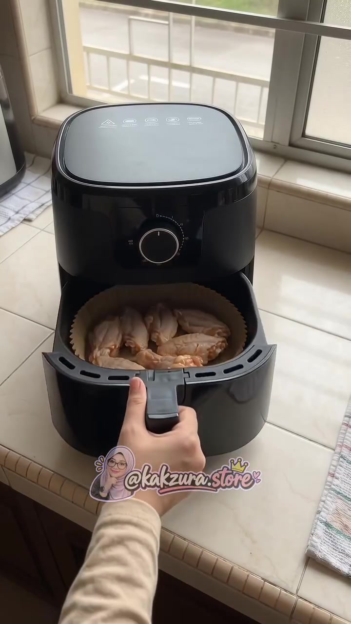 Drawer air fryer hitam dibuka menunjukkan pelapik kertas bulat berisi kepak ayam mentah sedia dimasak bersama kertas