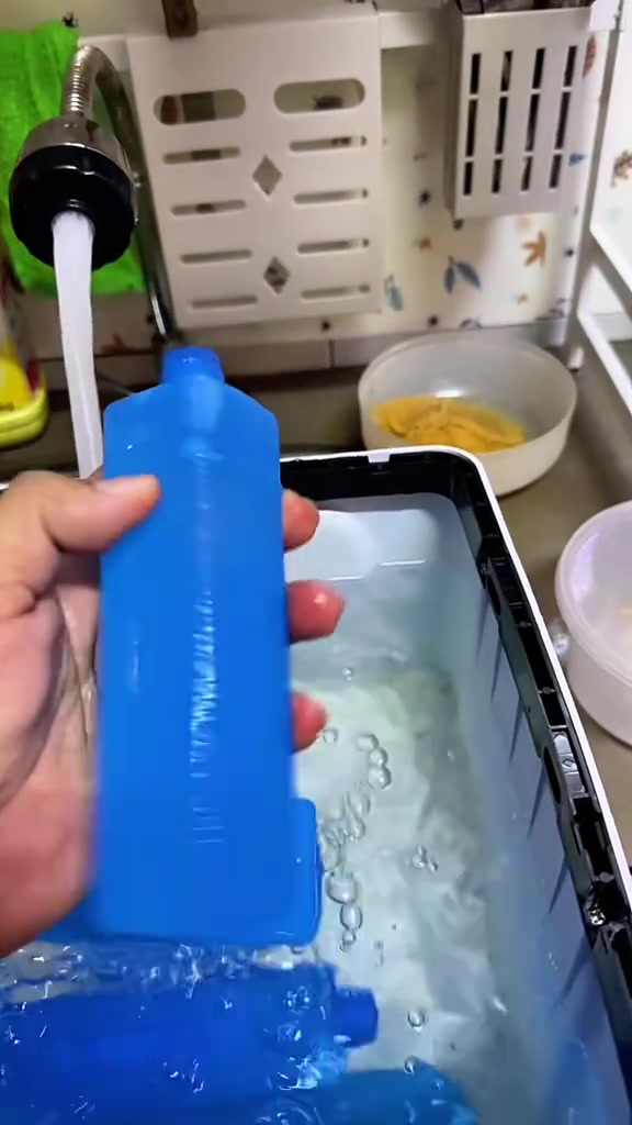 Tangan pegang ice pack biru di atas tangki air cooler yang berisi air