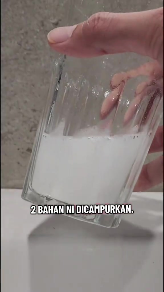 Tangan memegang gelas berisi campuran putih dua bahan pencuci yang dicampur