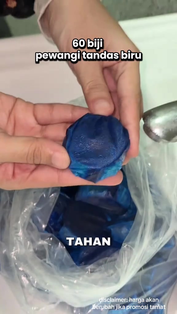 Tangan memegang sebiji blok flush tandas biru di atas beg plastik berisi banyak blok biru