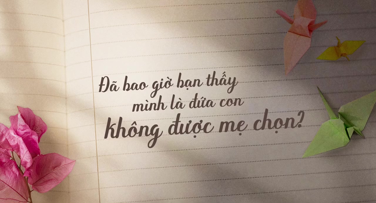 Card chữ trong teaser trailer Ngày Con Còn Mẹ trên nền giấy kẻ ngang: đã bao giờ bạn thấy mình là đứa con không được mẹ chọn, bên cạnh là hạc giấy và hoa giấy