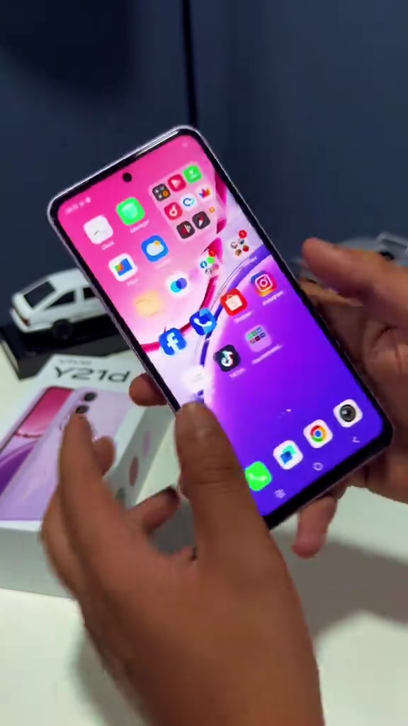 Skrin vivo Y21d yang hidup papar deretan ikon aplikasi pada Funtouch OS, dipegang dua tangan di atas kotak