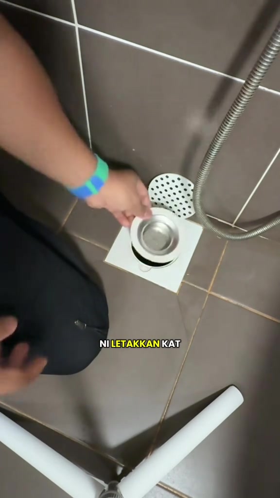 Tangan memasang insert penahan bau stainless steel ke dalam floor trap lantai bilik air