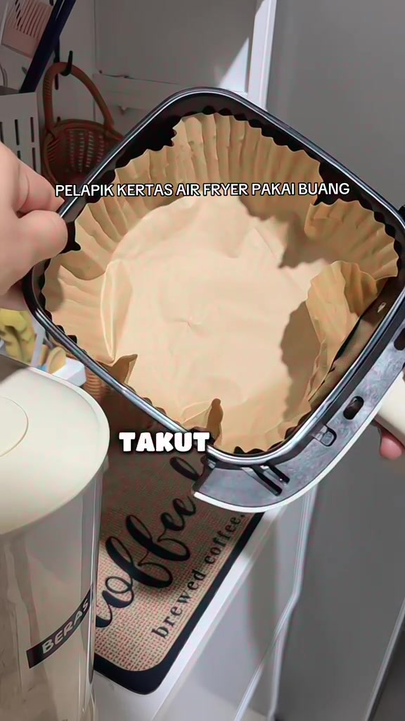 Bakul air fryer segi empat dipegang tangan dengan pelapik kertas parchment segi empat berlipat di dalamnya