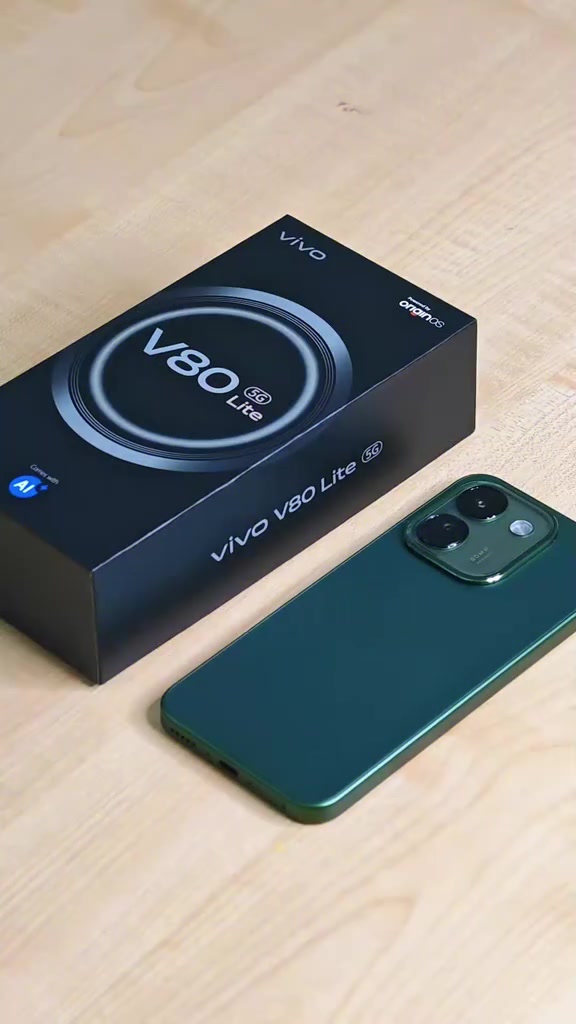 Kotak hitam vivo V80 Lite 5G di sebelah telefon hijau dengan modul kamera segi empat di atas meja kayu