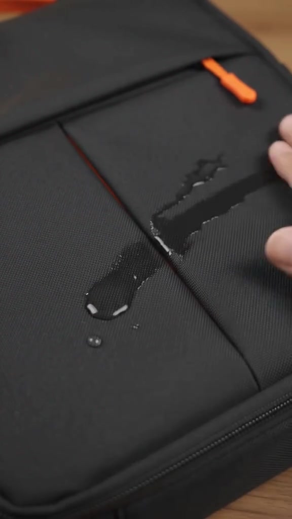 Titisan air kekal berbentuk bebola di atas fabrik hitam beg laptop, menunjukkan permukaan luar kalis air