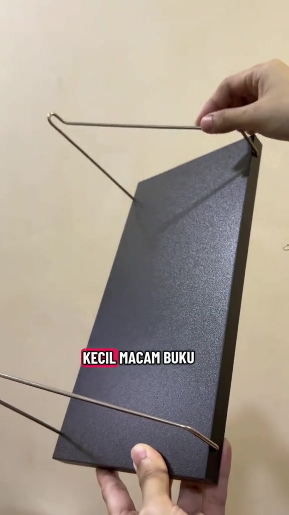 Tangan memegang papan rak hitam dari sudut bawah menunjukkan bracket wayar yang boleh dicangkum pada patch pelekat