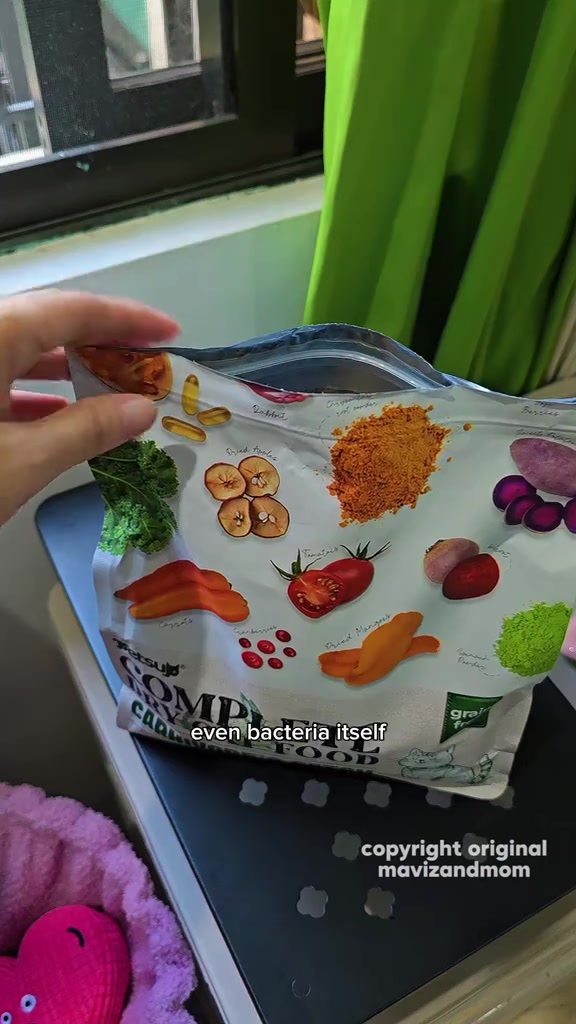 Tangan memegang bahagian atas beg makanan kucing yang sudah terbuka di atas bekas penyimpanan