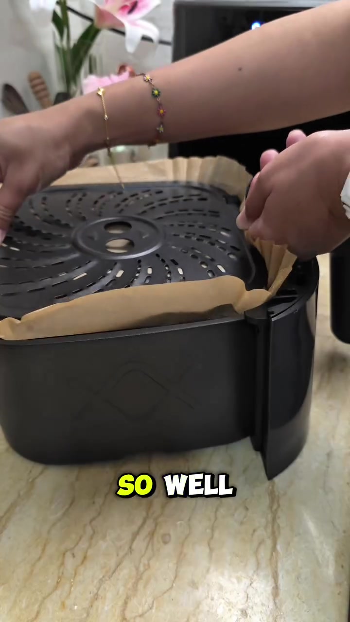 Tangan meletakkan plat grate berlubang hitam ke dalam bakul air fryer yang dindingnya dilapik kertas parchment