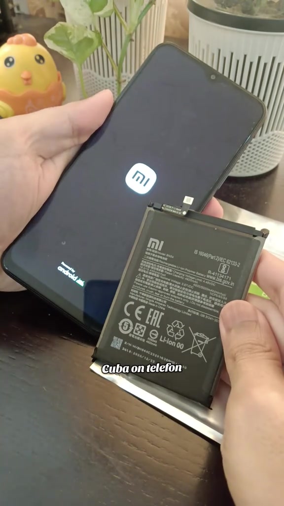 Bateri Xiaomi dipegang di sebelah telefon yang sedang but dengan logo Mi
