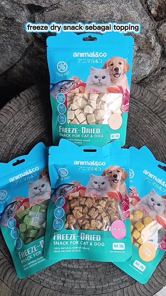 Beberapa pek snack freeze-dried Animal&Co warna turquoise dengan kiub chicken, salmon, egg yolk dan cat grass kelihatan pada tingkap pek