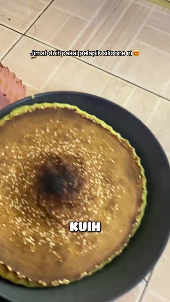 Kuih bakar pandan bertabur bijan baru masak di atas pinggan hitam dengan tepi pelapik silikon kelihatan di sisi