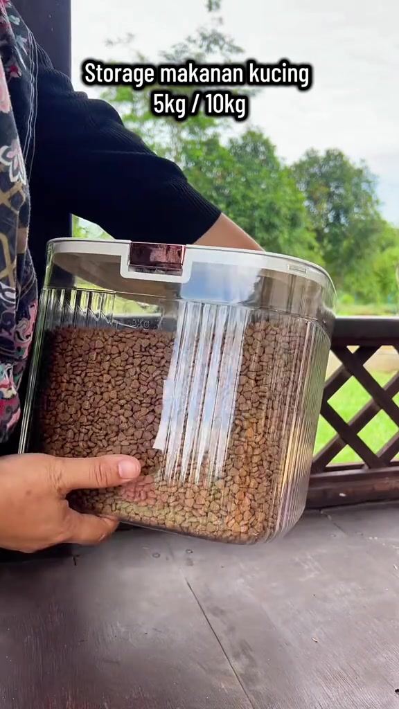 Bekas penyimpanan lutsinar kedap udara berisi kibbles dipegang dengan dua tangan, penutup putih berklip
