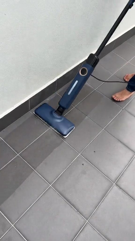Steam mop biru membersihkan lantai jubin kelabu rapat ke tepi dinding dan skirting