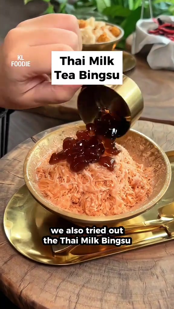Tangan menuang pearl ke atas bingsu perisa teh susu dalam mangkuk warna emas dalam kafe