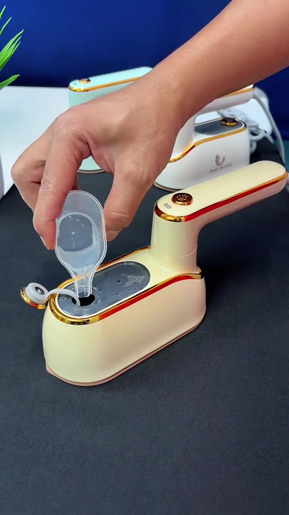 Tangan menuang air dari cawan penyukat kecil ke dalam tangki travel iron stim warna krim