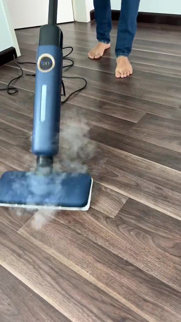 Kepala steam mop biru mengeluarkan wap di atas lantai laminate kayu, dengan skrin suhu bulat pada badan pemegang