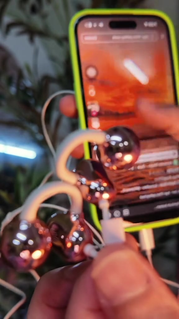 Earphone berwayar klip telinga rose gold di hadapan skrin telefon yang sedang mainkan muzik