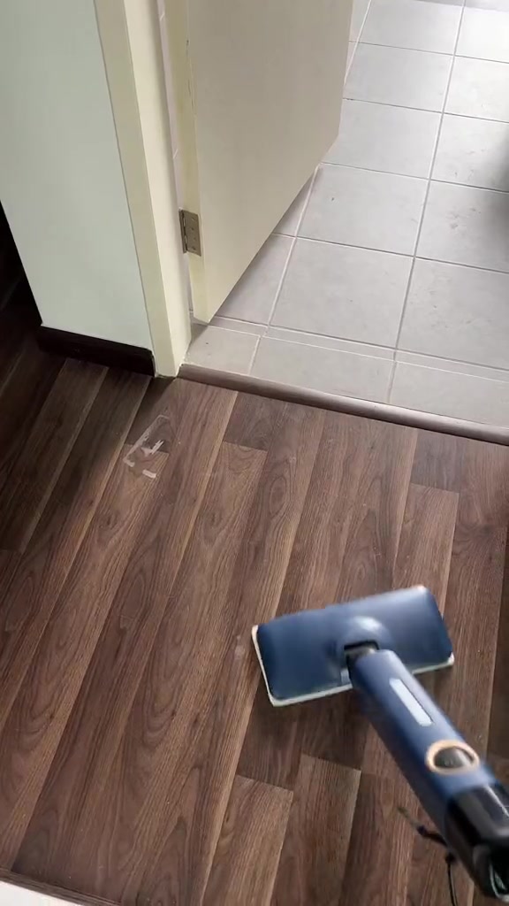 Kepala steam mop biru di atas lantai laminate rupa kayu berhampiran pintu bilik