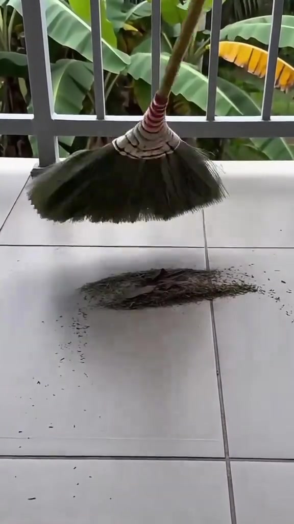 Penyapu jerami padi mengumpulkan longgokan daun kering dan habuk di lantai jubin putih, tiada orang dalam gambar