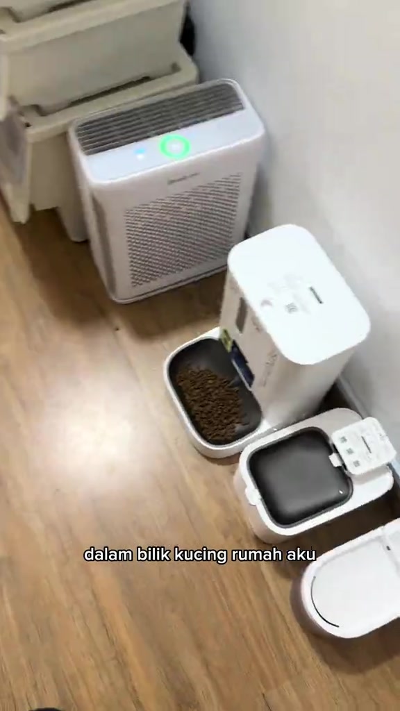 Barisan device elektrik bilik kucing: air purifier putih, auto feeder berisi kibbles dan water fountain di atas lantai kayu