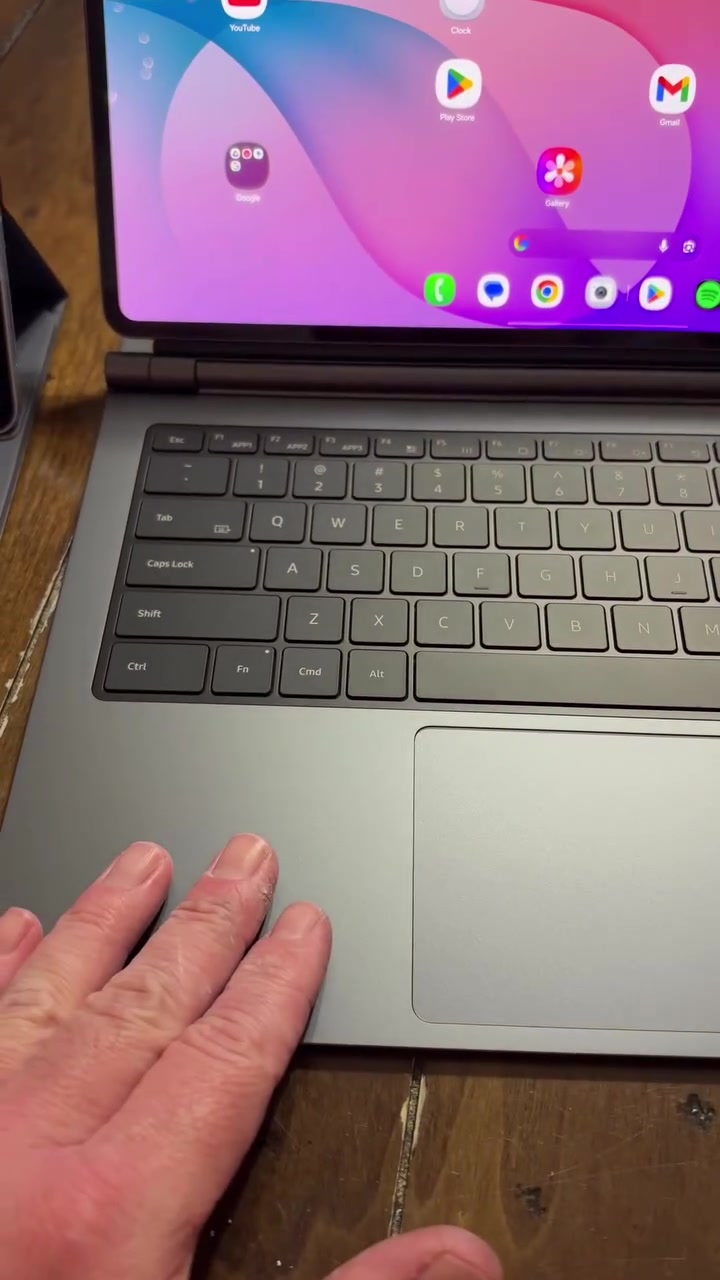Papan kekunci tablet berwarna kelabu dengan trackpad besar dan tangan diletakkan di sisinya, skrin tablet di belakang