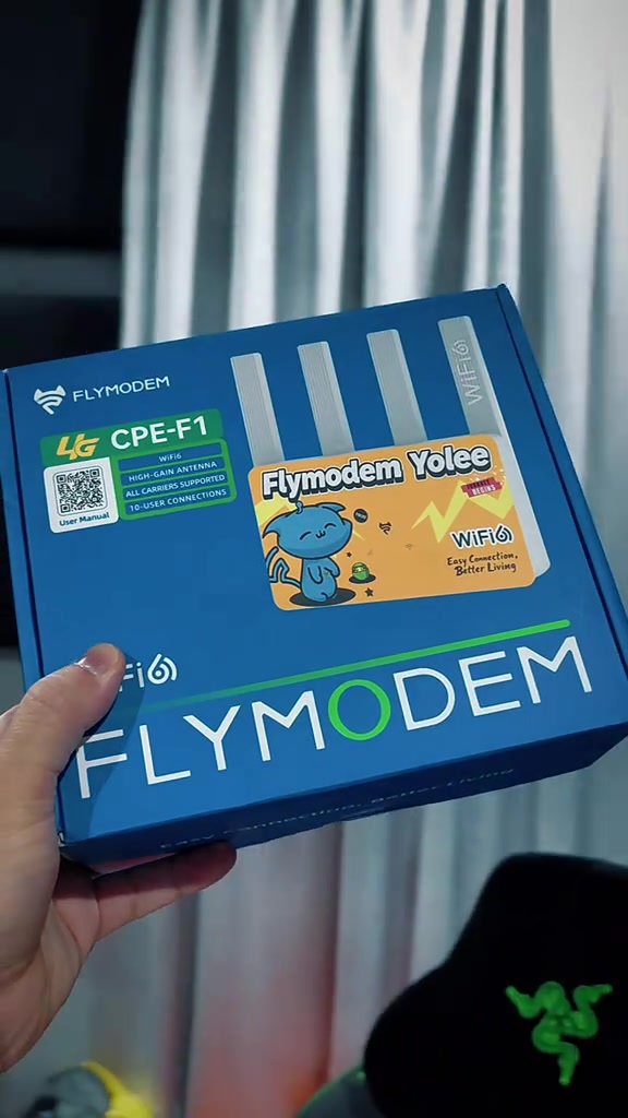 Kotak biru FlyModem CPE-F1 WiFi 6 dipegang tangan, dengan label empat antena, sokongan semua carrier dan sehingga 10 pengguna