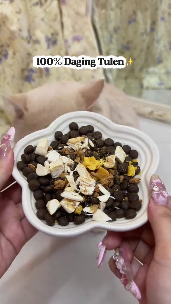 Tangan memegang mangkuk bentuk bunga berisi kibbles dengan freeze-dried topping di atasnya