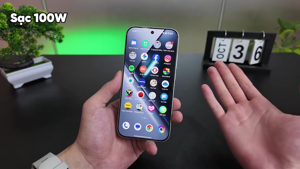 POCO X8 Pro cầm trên tay hiển thị màn hình chính, góc khung hình có chữ Sạc 100W