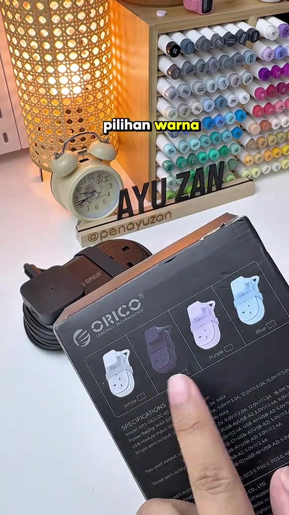 Kotak ORICO travel power strip menunjukkan empat pilihan warna dan spesifikasi model AP3-2A2U2C-65, unit coklat terlihat di belakang kotak