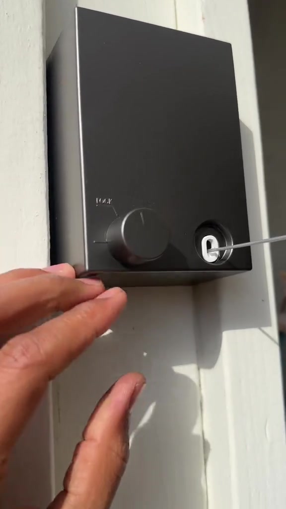 Tangkap dekat kotak retractable clothesline kelabu gelap pada dinding putih dengan knob lock dan dawai keluar dari lubang hadapan