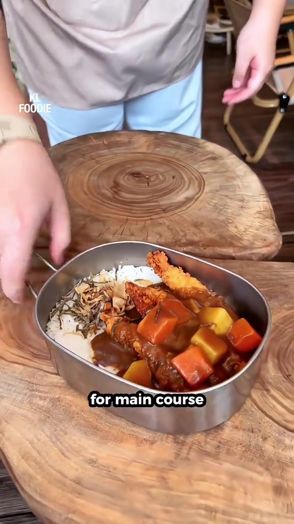 Tangan meletak bekas logam berisi nasi dengan kari ayam dan sayur atas meja kayu dalam kafe