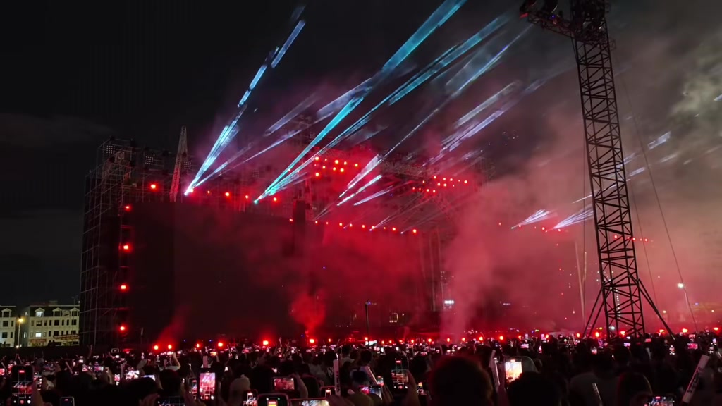 Khán giả nhìn từ phía sau giơ điện thoại quay sân khấu concert Anh Trai Vượt Ngàn Chông Gai 2026 giữa những chùm laser xanh quét dài và khói đỏ phủ kín sân khấu